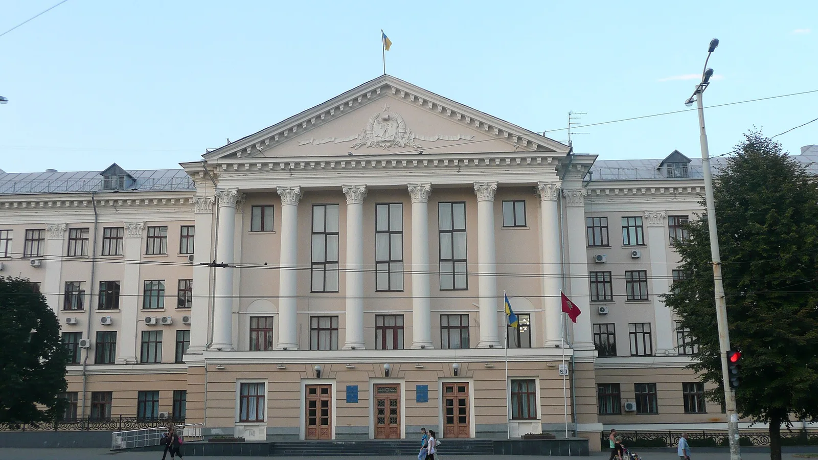 Фасад адміністративної будівлі з колонами, входом і прапором України на даху