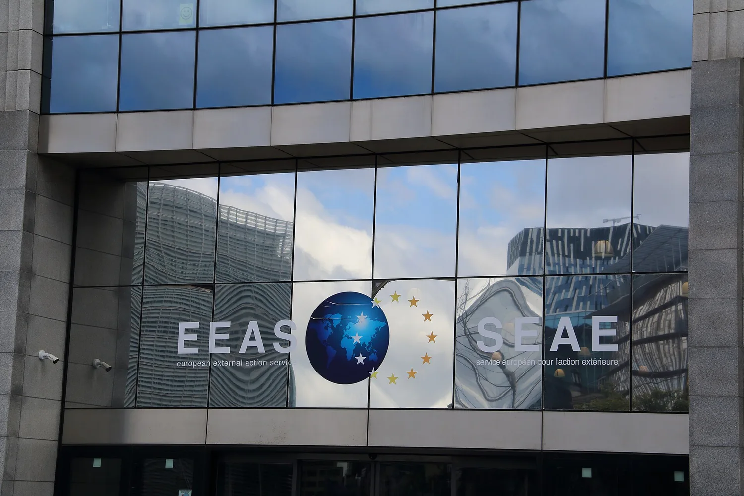 Фасад будівлі з написом EEAS на скляній стіні та відбиттям сусідніх будівель