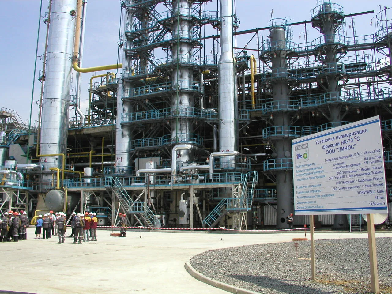 Нафтопереробний завод з трубами та технологічними колонками; люди у спецодязі на передньому плані