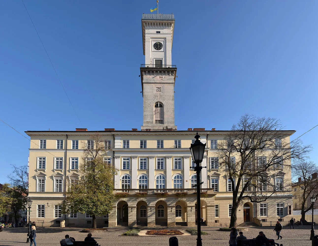Ратуша Львова на Площі Ринок з годинниковою вежою, ясне блакитне небо, кілька людей на площі