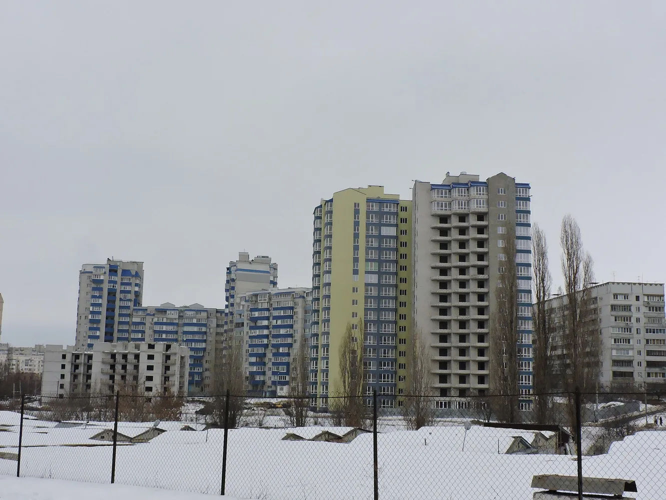 Багатоповерхові житлові будинки на сніжній ділянці в Харкові, панорама вулиці з кількома житловими висотками.