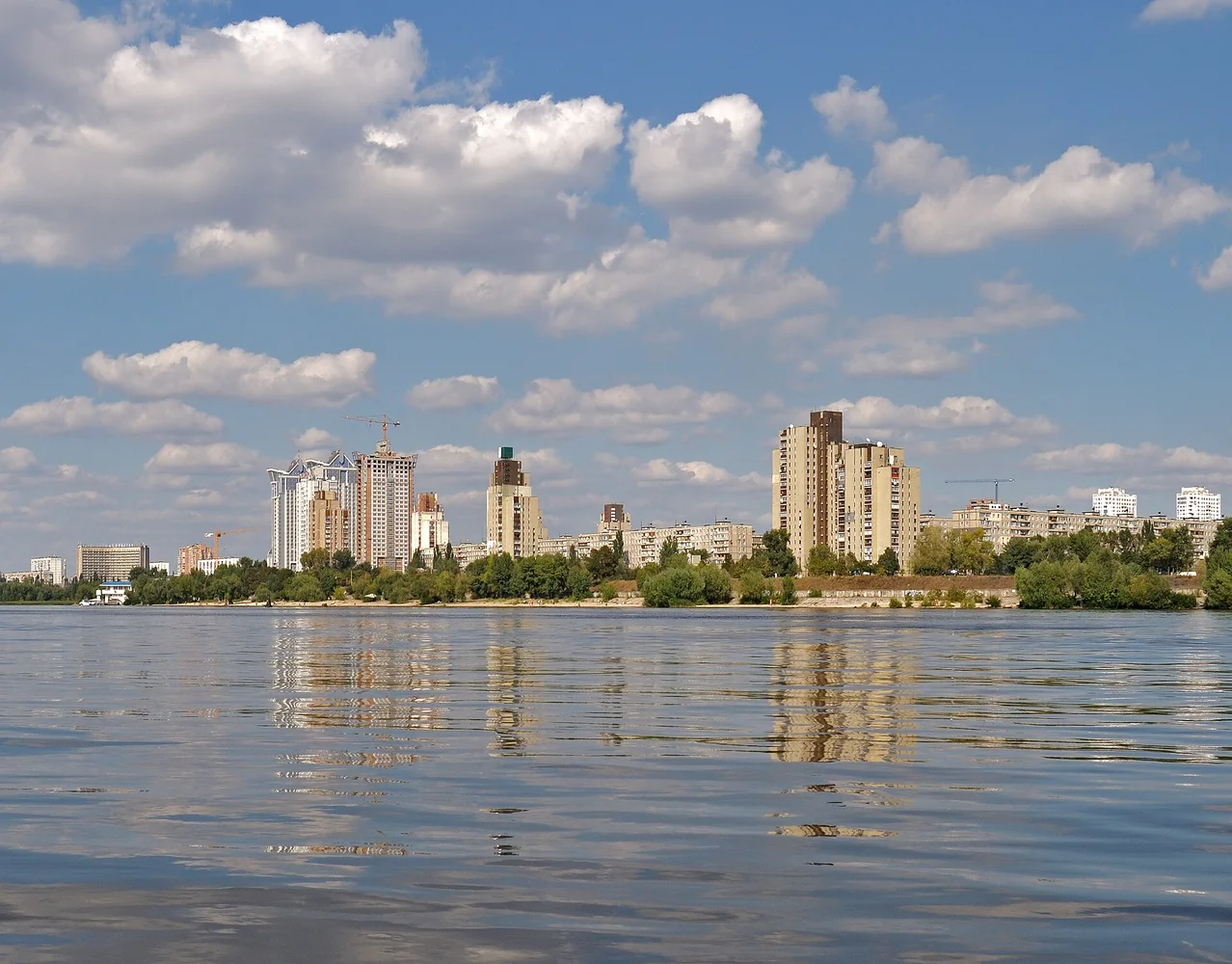 Дніпровський берег у Києві з видом на високі багатоповерхівки та віддзеркалення у воді