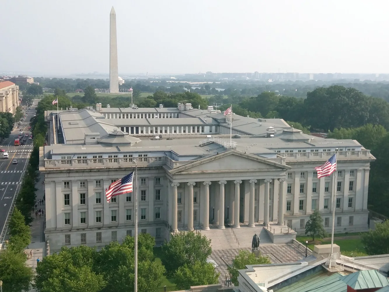 Фотографія будівлі Міністерства фінансів США у Вашингтоні з Вашингтонським монументом на задньому плані.