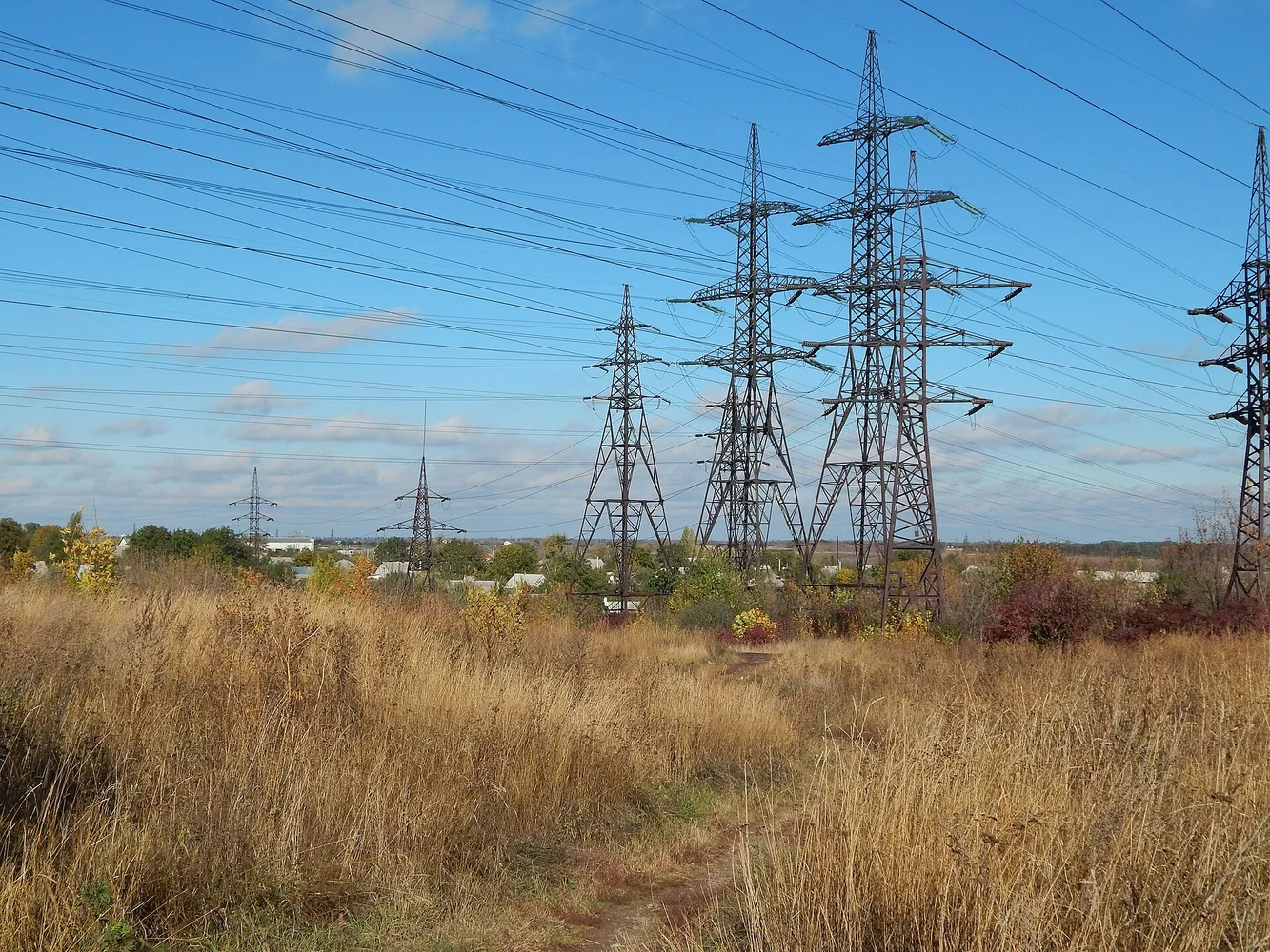 Лінії електропередач і металеві опори високовольтних трансмісій на фоні осіннього поля та неба.