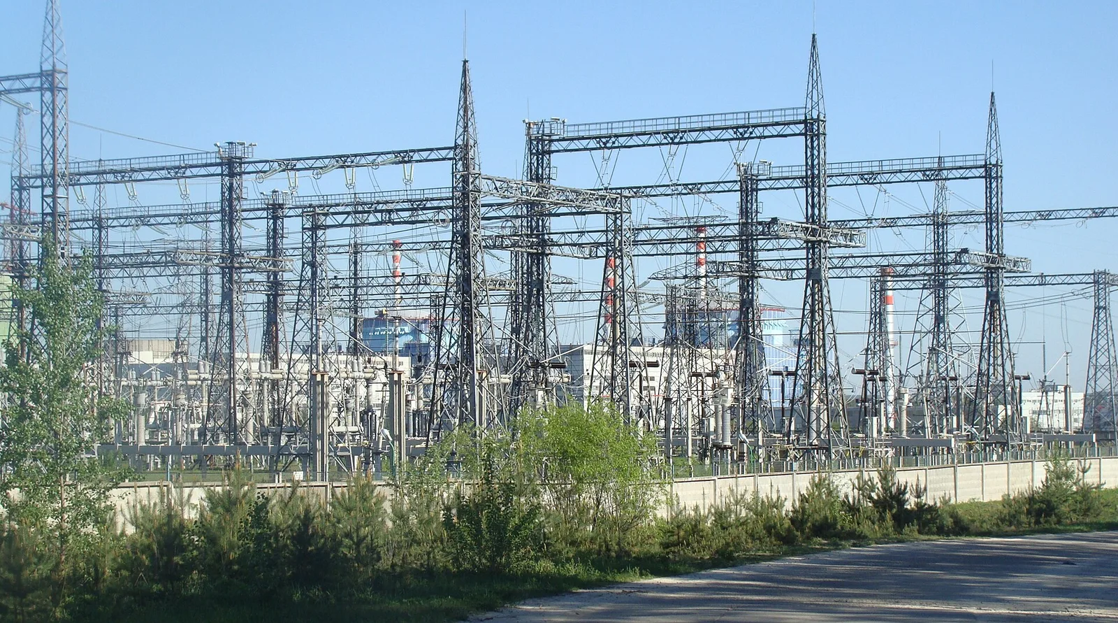 Високовольтна електрична підстанція з металевими опорами, трансформаторами та проводами на тлі ясного неба.