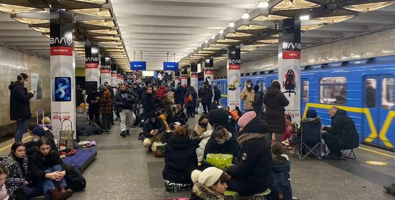 Платформа київського метро, багато людей сидять і стоять на підлозі поруч із поїздом, використовують станцію як укриття